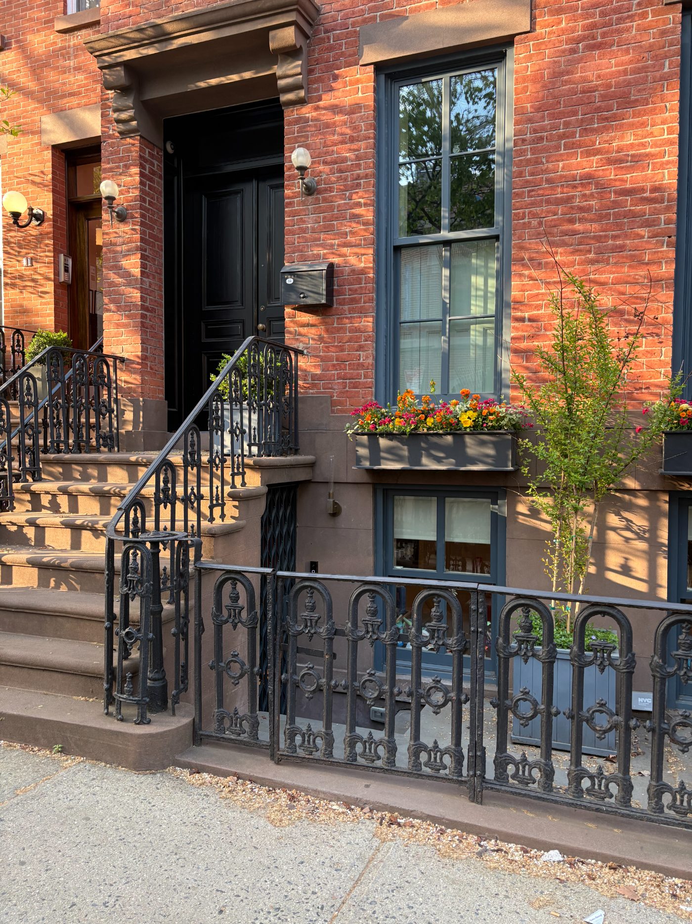 A planted brownstone entry — iron railings, flower box, and bluestone stoop — the architectural language Stoop is drawn from.